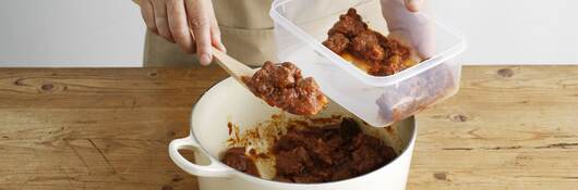 Woman spooning food into a plastic container.