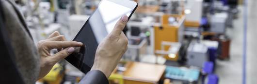 Manager reviewing a tablet while overlooking a factory floor