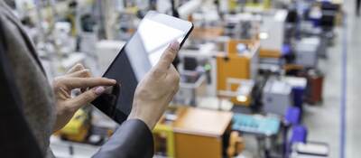 Manager reviewing a tablet while overlooking a factory floor