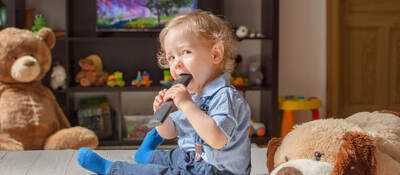 Toddler sitting while chewing on a tv remote