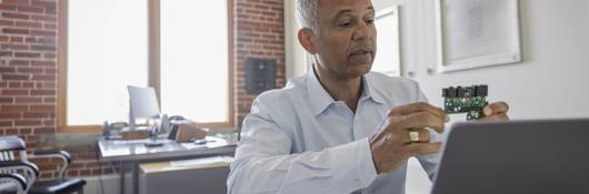 Male engineer at laptop explaining semiconductor on video call in meeting.