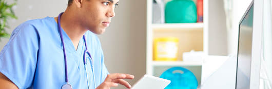 A medical professional reading a chart on a tablet and desktop monitor