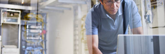 Man using a laptop with an IT server in the background