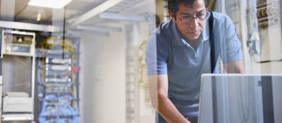 Man using a laptop with an IT server in the background