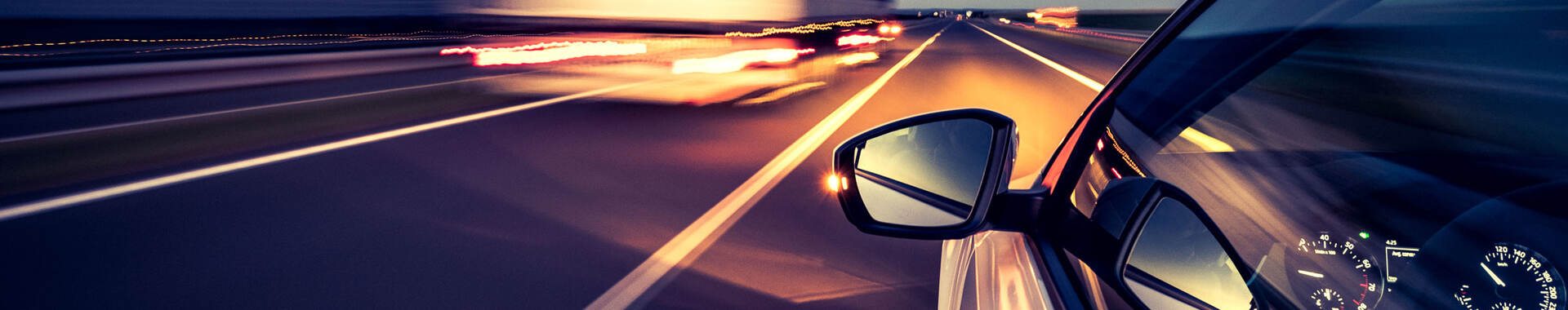 Silver car with side-view mirror driving on highway beside heavy duty truck at night