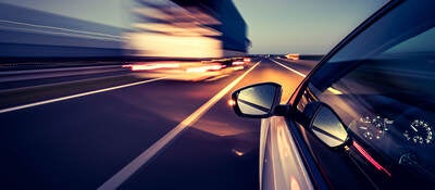 Silver car with side-view mirror driving on highway beside heavy duty truck at night